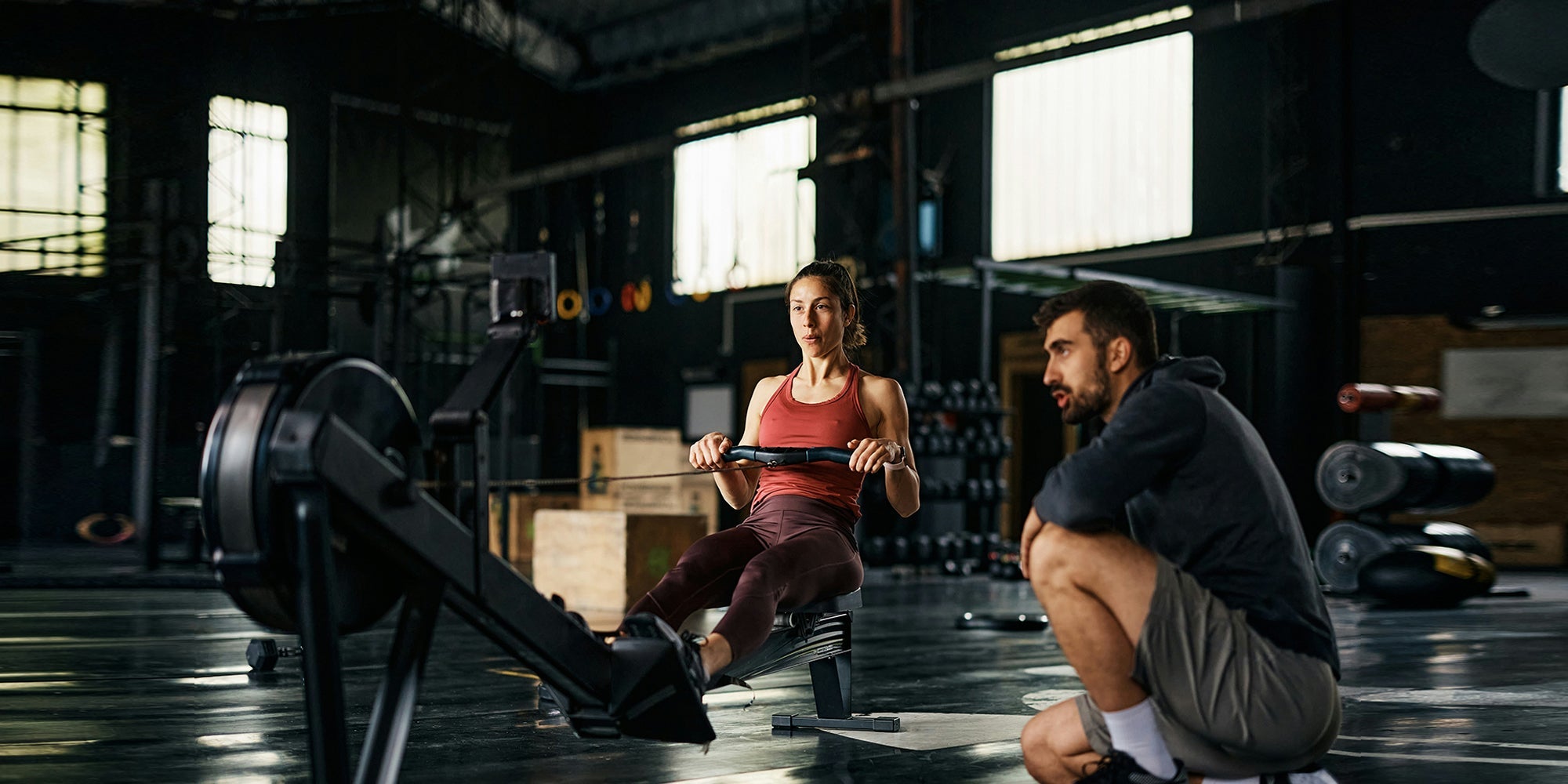 a woman rows on a rowing machine while a man watches