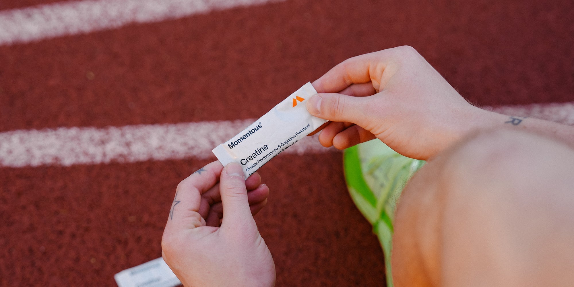 athlete at track holding creatine travel pack